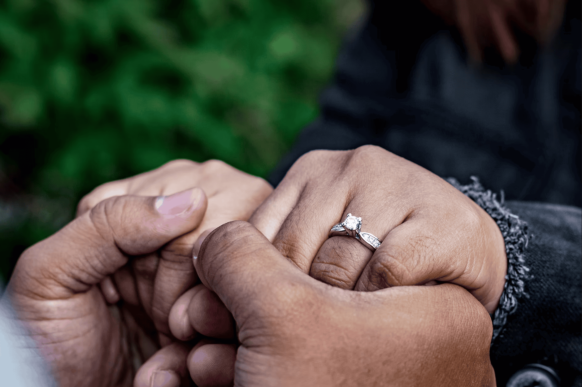 Close-up of couple holding hands with a sparkling diamond engagement ring